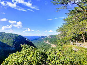 A vista of green, tree covered hills, with a blue sky and some clouds overhead.